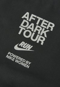 Black fabric featuring bold white text: "AFTER DARK TOUR RUN" and "POWERED BY NIKE WOMEN," with a Nike logo.