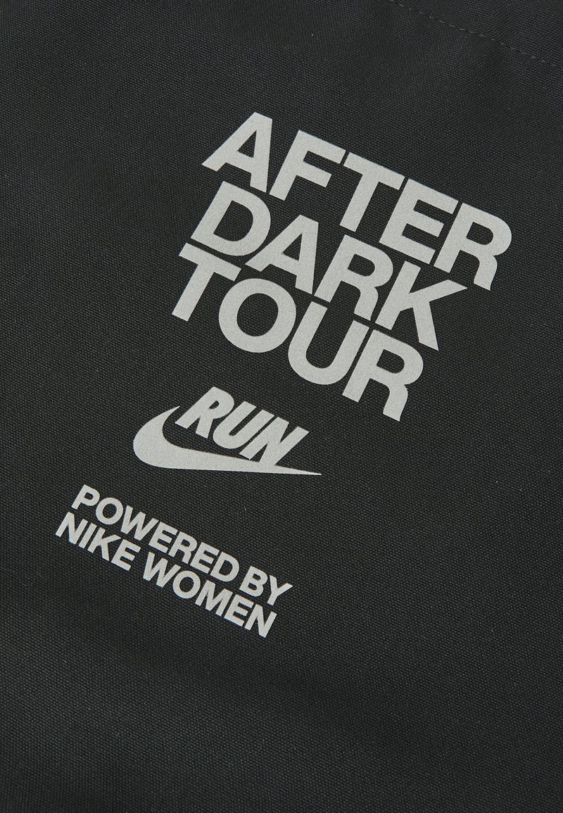 Tissu noir avec un texte blanc audacieux : "TOUR APRES L'OBSCURITE" et "PROPULSÉ PAR NIKE WOMEN," avec un logo Nike.