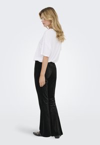 Maglietta bianca oversize abbinata a pantaloni a zampa neri in velluto a vita alta. Tessuto liscio e vestibilità rilassata, completati da calzature nere.