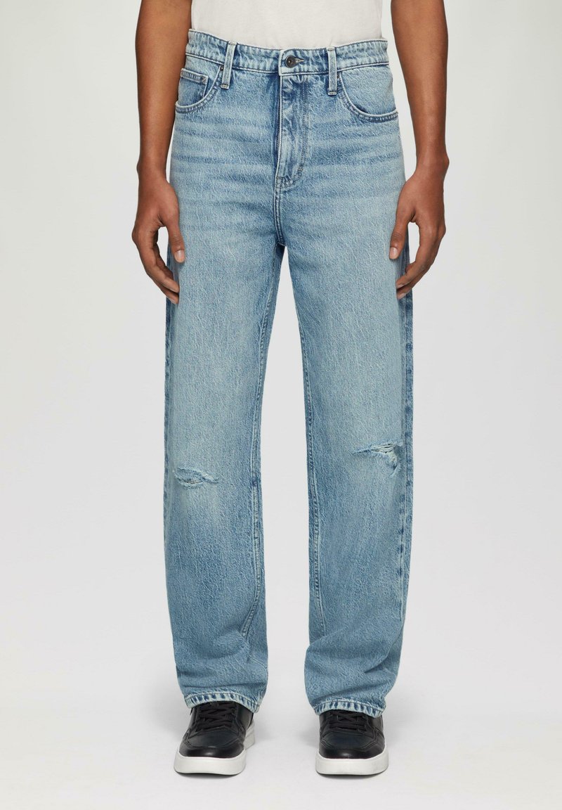 Jean en denim bleu clair avec une coupe décontractée, présentant des détails déchirés au niveau des genoux, un design à cinq poches et des coutures contrastées.