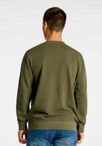 Grön sweatshirt i mjukt tyg med långa ärmar, rund halsringning och ribbad mudd. Matchad med blå jeans.