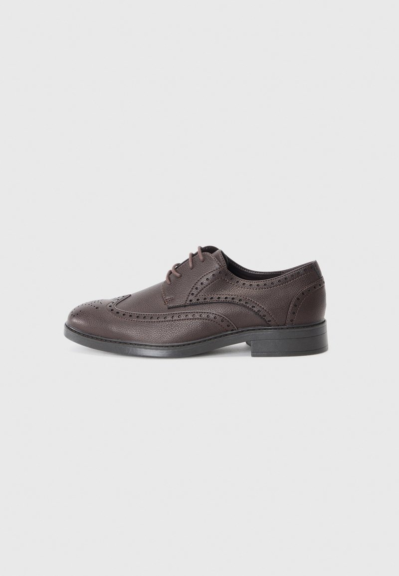 Chaussure habillée en cuir marron foncé avec des détails brogues et une semelle noire, vue de côté sur un fond gris uni.