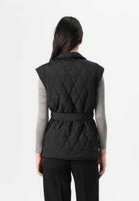 Gilet matelassé noir avec une taille ceinturée, doté d'un col et sans manches. Texture lisse avec un motif en losanges sur le tissu.