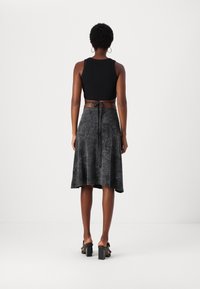 Schwarzes, croptop mit einem langen, grauen, strukturierten Rock, der eine Bindung an der Taille hat. Model trägt schwarze Blockabsatzsandalen.