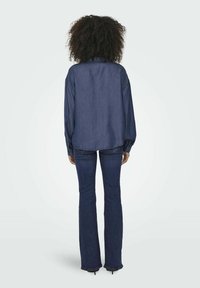 Camicia in denim blu scuro con maniche lunghe, polsini bottonati e orlo curvo, abbinata a jeans blu scuro a zampa d'elefante e tacchi neri.