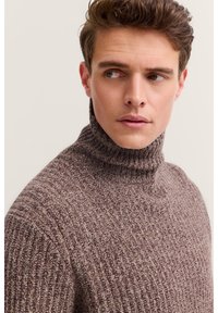 Brauner gerippter Rollkragenpullover mit strukturiertem Strickmuster. Der Kragen ist hoch, und der Stoff wirkt weich und dick.
