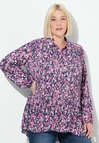 Blusa floral en tonos de rosa, blanco y azul marino, con cuello abotonado, textura plisada, mangas largas y un corte relajado.