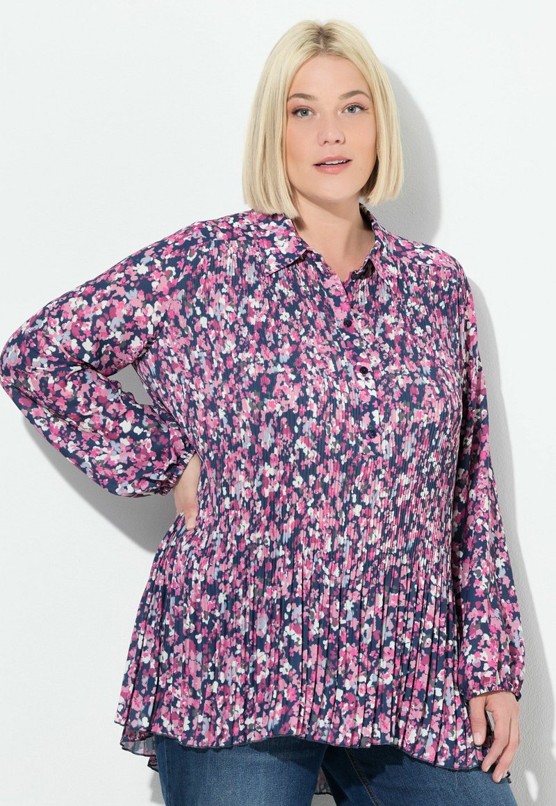 Blusa floral en tonos de rosa, blanco y azul marino, con cuello abotonado, textura plisada, mangas largas y un corte relajado.