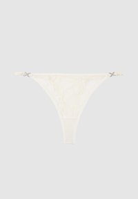 String en dentelle blanche avec fines bretelles latérales ornées de petits nœuds décoratifs de chaque côté.
