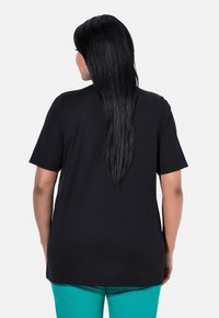 Camiseta negra de manga corta con un ajuste relajado, textura suave y cuello redondo básico, combinada con pantalones en tono azul verdoso.