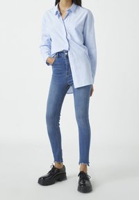 Camisa de botón azul claro con un bolsillo, combinada con jeans ajustados de talle alto en azul. Zapatos de plataforma negros con detalles de cordones.