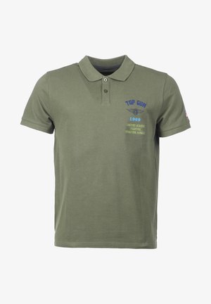Olivi vihreä polo-paita, joka on valmistettu puuvillasta. Siinä on kaulus ja kolmen napin napitus. Etupuolella on brodeerattu "TOP GUN" -teksti sekä lisäteksti.