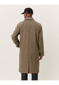 Lång, rutig kappa i brunt och beige med subtila röda och gröna accenter. Har en klassisk krage och knäppta manschetter.