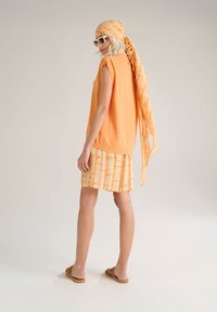 Top arancione senza maniche con una vestibilità comoda, abbinato a una gonna con fantasia in tonalità più chiare. Gli accessori includono una sciarpa coordinata.