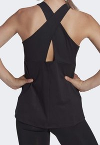 Débardeur de sport noir avec une texture côtelée, doté d'un design croisé dans le dos et d'une découpe au niveau du haut du dos. Ourlet lisse, coupe ajustée.