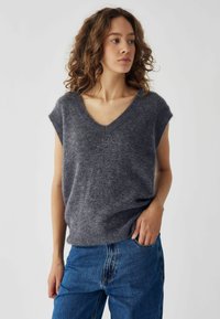 Suéter gris de manga corta y cuello en V, hecho de un tejido suave y texturizado, combinado con jeans de denim azul. Ajuste simple y relajado.