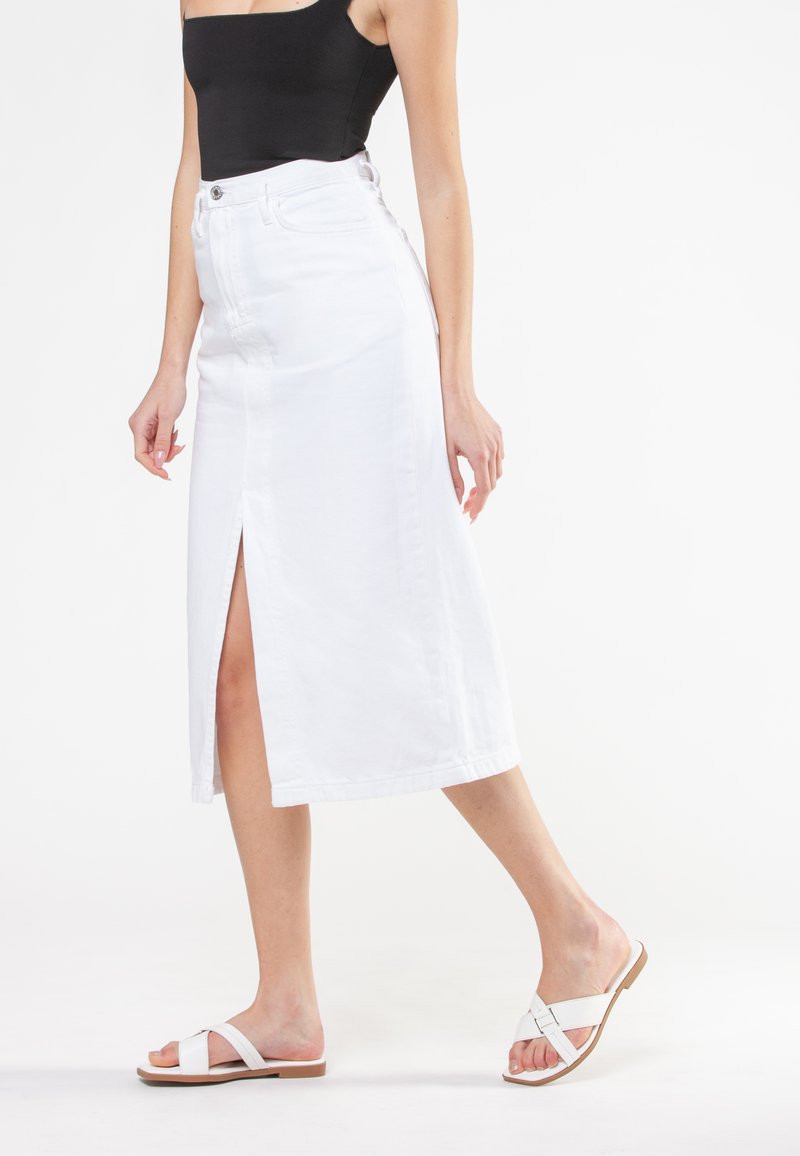Hvid denim midi-nederdel med en frontslids, høj talje og fem-lomme design. Parret med flade, hvide sandaler med et minimalistisk strop.
