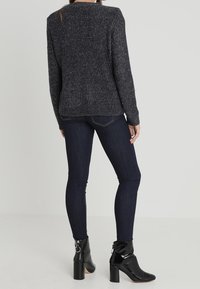 Dunkelgrauer Strickpullover mit strukturierter Oberfläche, kombiniert mit dunkelblauen Skinny-Jeans und schwarzen Stiefeletten mit Blockabsatz und Schnallen-Detail.