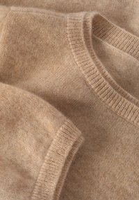 Beige gebreide trui met een ronde halslijn, geribbelde manchetten en een zachte textuur met een gemêleerd patroon.