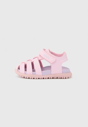 Sandalia de goma rosa con diseño de punta cerrada y correa ajustable. Presenta detalles recortados, suela texturizada y plantilla en lavanda contrastante.