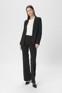 Blazer nero su misura, t-shirt bianca sotto, pantaloni neri a vita alta e décolleté neri con punta affilata. Tessuto morbido, design minimalista.