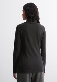 Melnā garo piedurkņu turtleneck blūze ar gludu tekstūru un pieguļošu dizainu, kurai ir smalks logo tagiņš pie apakšmalas.