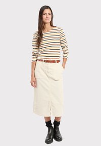 Gestreepte lange mouw top in beige, bruin en geel, gecombineerd met een crèmekleurige corduroy rok. Heeft een voorkantsplit en een bruine riem, gedragen met zwarte laarzen.