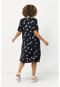 Marinekleid mit weißen Punkten, kurzen Ärmeln, lockerer Passform, knielang, glatter Textur und rundem Ausschnitt. Die Schuhe haben Riemen und Plateau-Sohlen.