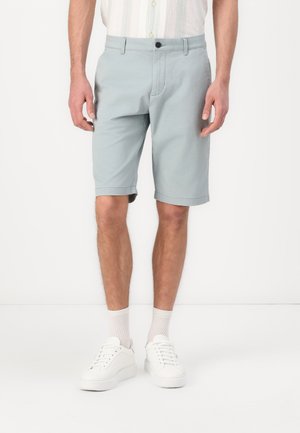Lyseblå shorts laget av en bomullsblanding, kne-lange med knappelukking, brukt med hvite sneakers og lyse sokker.