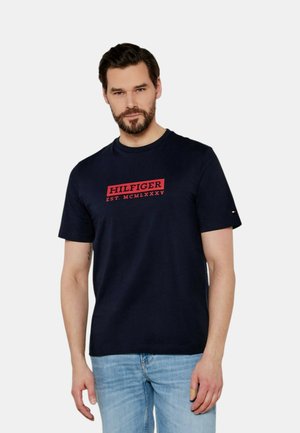 T-shirt in cotone blu navy con stampa rossa "HILFIGER EST. MCMLXXXV", maniche corte e scollo a girocollo con un logo accentato sulla manica.