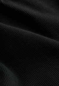 Gros plan sur un tissu noir côtelé montrant des lignes texturées et des plis doux à la surface du matériau.