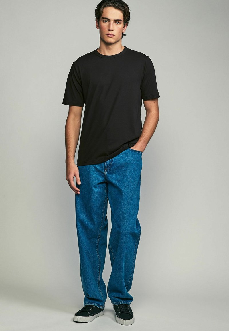 Camiseta negra de manga corta combinada con jeans de denim azul. Los jeans tienen un corte relajado y el conjunto se completa con zapatillas negras.