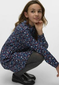 Abito floreale con base blu navy, caratterizzato da fiori rossi, bianchi e blu. Abbinato a collant grigi e mocassini neri. Maniche lunghe, vestibilità rilassata.