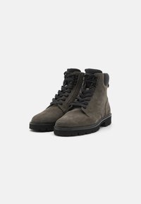 Bottines en daim gris avec des lacets noirs, semelles en caoutchouc et un panneau arrière texturé. Dotées d'un soutien de cheville renforcé et de détails œillets.