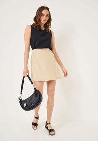 Haut sans manches noir, jupe évasée beige, sac à main noir et sandales noires. Tissu lisse, design simple et accents minimaux.