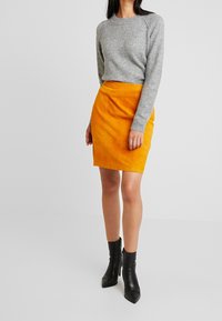 Maglione grigio a maglia con scollatura rotonda, abbinato a una gonna gialla in suede a vita alta e stivaletti neri con punta affusolata.