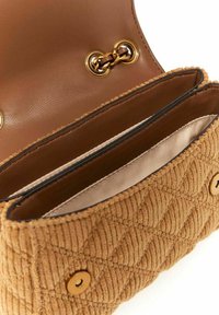 Sac à main en velours côtelé marron avec un motif texturé et matelassé, des accessoires en or et un intérieur en cuir lisse. Il dispose d'une fermeture à pression et de deux compartiments.