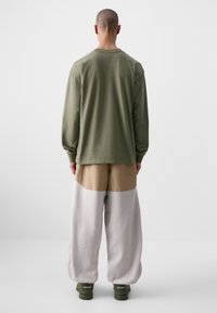 Olíva zöld, hosszú ujjú ing bézs és világosszürke, oversized nadrággal párosítva, amely laza szabású és puha anyagú.