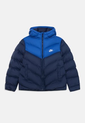 Casaco puffer azul marinho e azul brilhante com capuz, apresentando um design em chevrão, fecho zip e logótipos da Nike em branco na parte superior frontal.