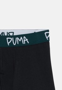 Biancheria intima nera con un elastico verde scuro che presenta il logo del marchio PUMA in lettere bold bianche.