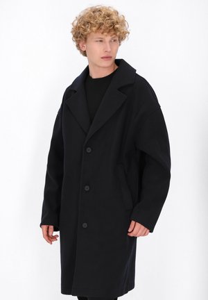 Schwarzer Wollmantel mit Reverskragen, oversized Passform, einreihiger Knopfverschluss und seitlichen Taschen. Glatte Textur, minimales Design.