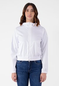 Giacca cappuccio bianca con zip, realizzata in materiale leggero e liscio. Presenta polsini ed elastiche in vita, e tasche frontali per la praticità.