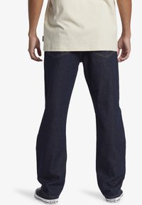 Mörkblå denimjeans med en lös passform, raka ben och två bakfickor. Matchas med svarta lågtoppade Converse-sneakers.