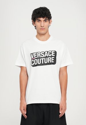 Hvit bomulls t-skjorte med iøynefallende svart "VERSACE JEANS COUTURE"-logo. Klassisk rund hals og korte ermer som gir en avslappet passform.