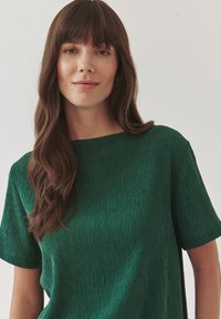 Groen getextureerd shirt met korte mouwen, een losse pasvorm en een bootnek, met een subtiele kreukpatroon door de stof.