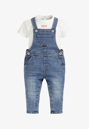 Camicia bianca a maniche corte con scritte rosse sotto salopette da bambino in denim blu con tasca frontale e bretelle con bottoni.