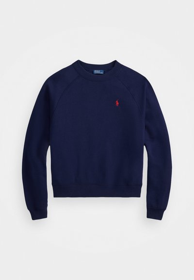 Granatowy sweter z ribbowanymi mankietami i dołem, okrągłym dekoltem oraz małym czerwonym logo po lewej stronie klatki piersiowej. Wykonany z miękkiego materiału bawełnianego.