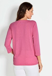Rosa, leichtes Langarmshirt mit lockerer Passform und runder Halslinie. Der Stoff hat eine subtile Textur und wird mit weißen Hosen getragen.