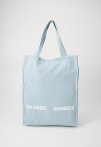 Šviesiai mėlynas drobės tote krepšys su dviem baltais „SAM SøE“ logotipais. Yra du tvirti rankenos ir paprastas stačiakampis dizainas.