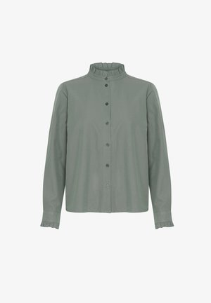 Zaļš krekls ar pogām, ar rufflētu apkakli un aprocēm, ar gludu tekstūru un garām piedurknēm. Pogas ir tumšas ar vienkāršu dizainu.